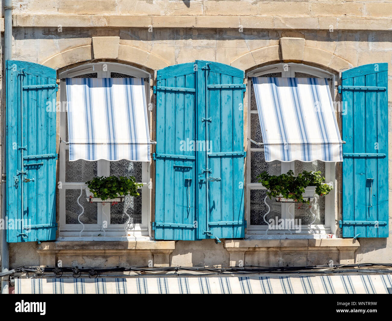 Windows framed by beautiful blue shutters and awnings. Stock Photo