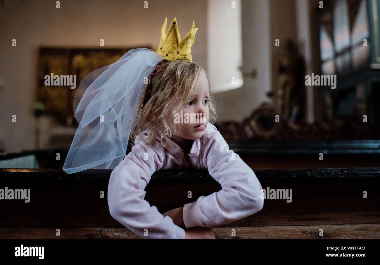 girl sat with a dress up crown & veil on her head, looking thoughtful Stock Photo