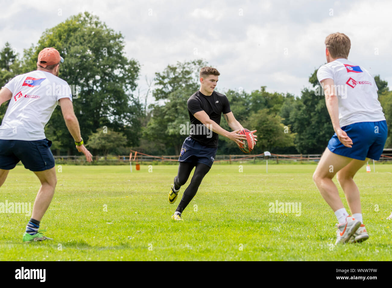 Amateur touch rugby player (male, 20-30 y) prepares to pass the ball to teammate, as two opponents face him to make the tackle Stock Photo
