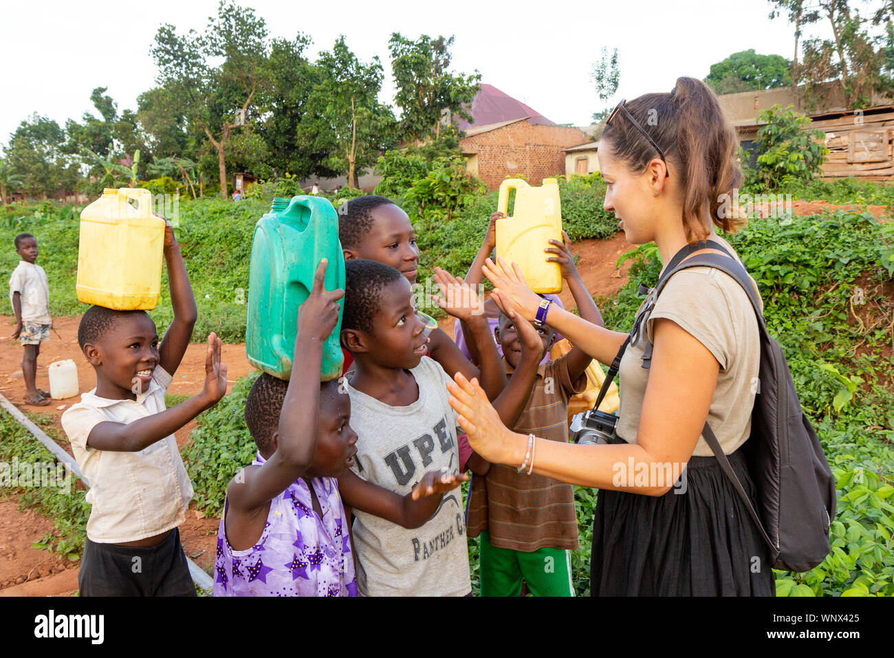 A white-skinned volunteer (called 'mzungu' or 'muzungu' by the locals) talking to Ugandan children on a railway track in a rural area. Stock Photo