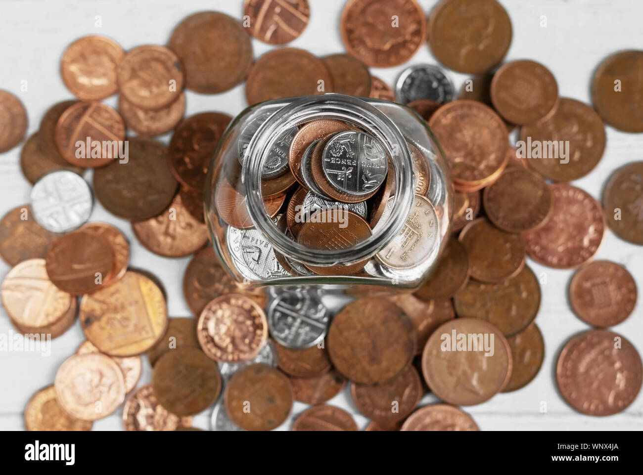 Full jar of coins from above, surrounded by loose change. Money saving and investment concept Stock Photo