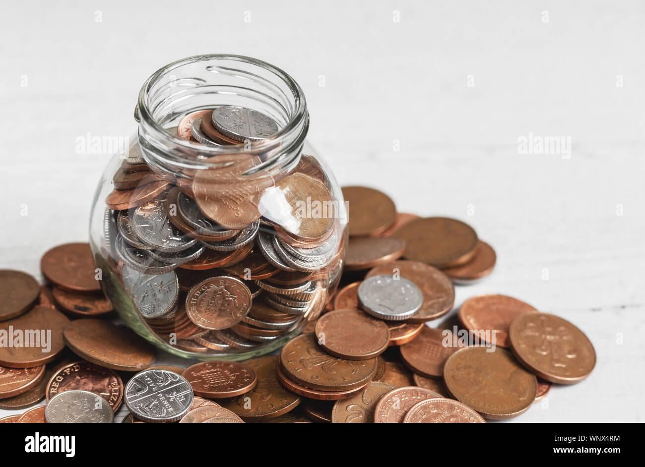 Full jar of coins on a table, surrounded by loose change. Money savings concept with copy space ...