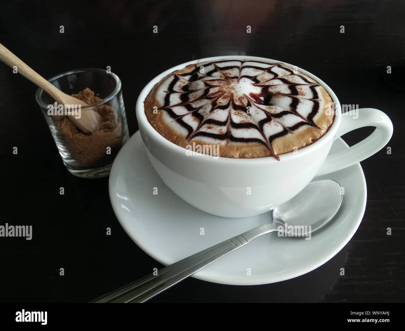 Hot coffee latte with latte art milk foam in cup mug on black wood desk on  top view. As breakfast In a coffee shop at the cafe,during business work  concept Stock Photo