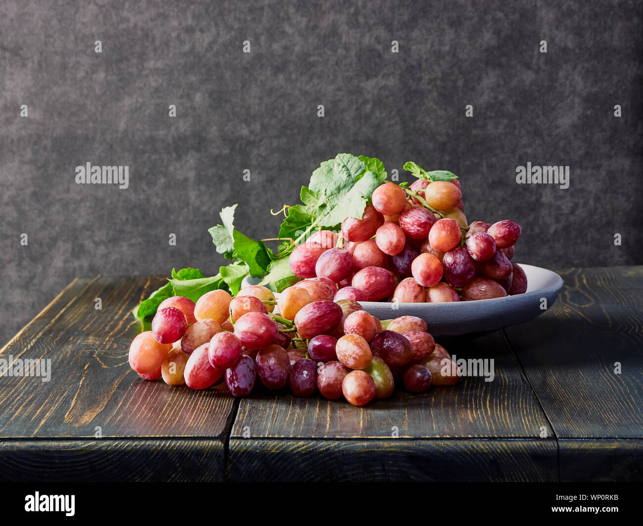 Fresh grapes. Bunches of different varieties in a plate on an old wooden table and dark background. soft focus Stock Photo