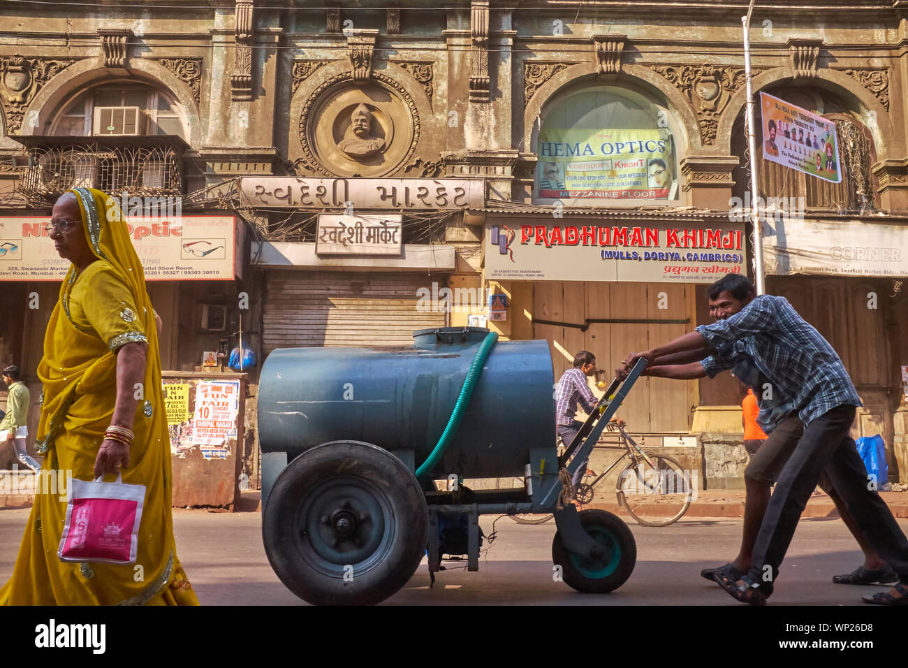 Workers pushing a 500 liter water tanker along Kalbadevi Rd. in business area Bhuleshwar, Mumbai, India, where many buildings have no running water Stock Photo