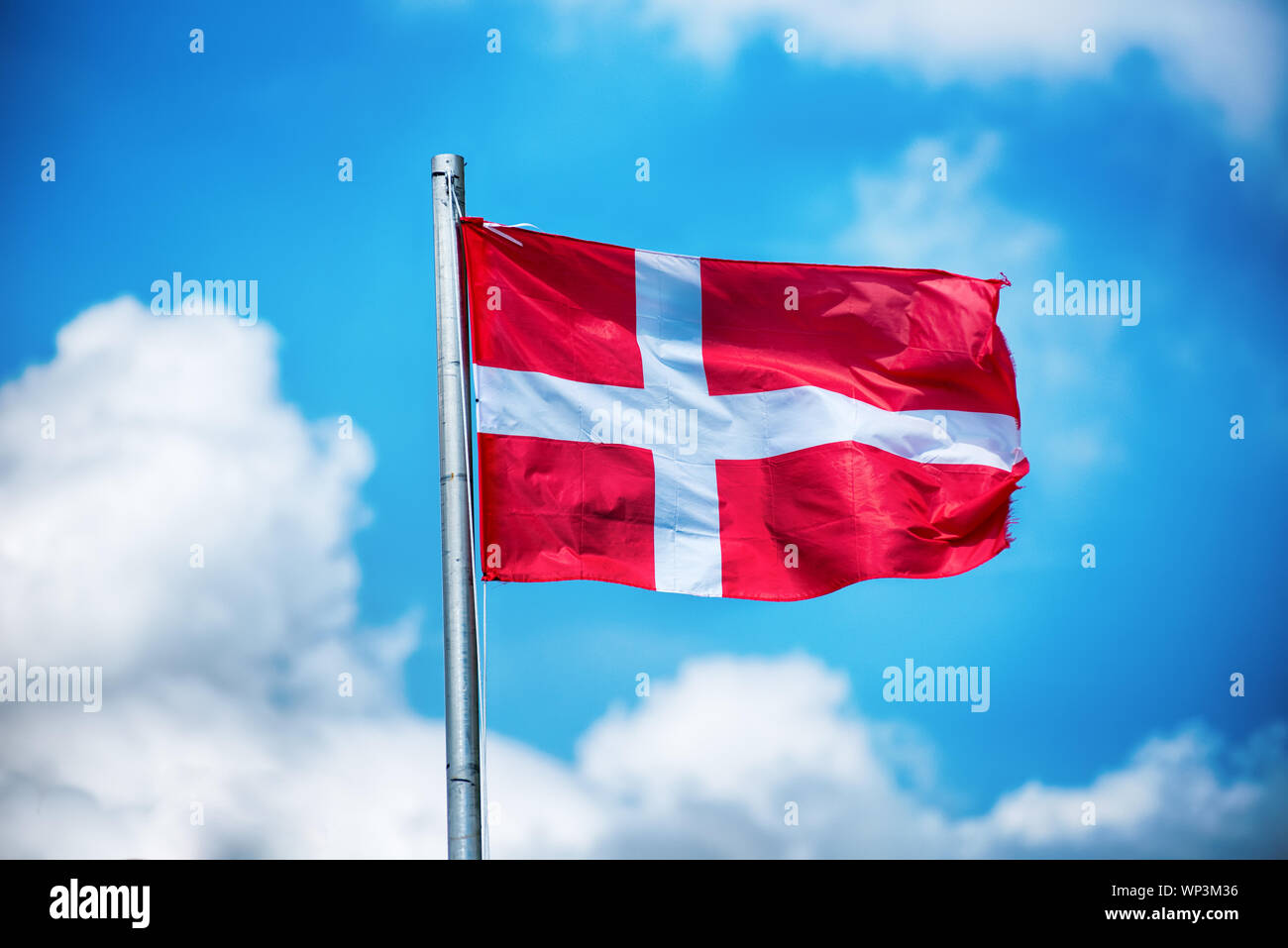 National flag of Denmark fluttering in the wind on a flagpole against a sunny blue sky with fluffy white cloud Stock Photo