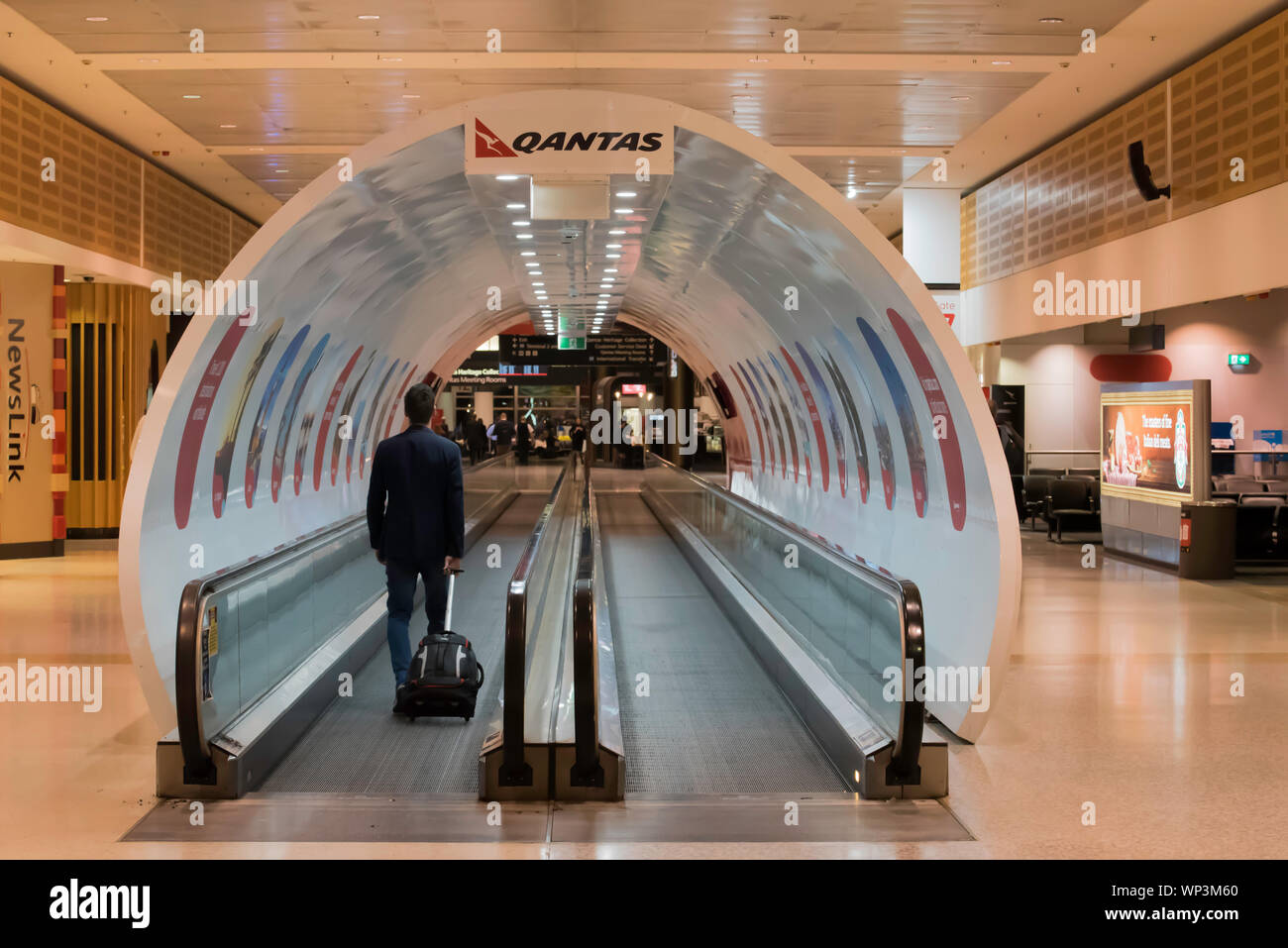 A traveler rides on a moving walkway in the Qantas Sydney Domestic Terminal covered by a fake Qantas jet airplane at Sydney's Kingsford Smith Airport Stock Photo