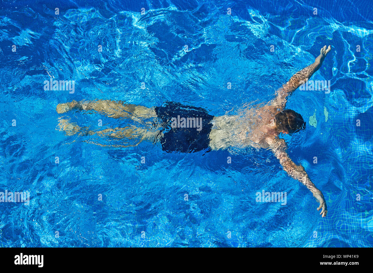 Teenage boy in black swimming trunks swimming underwater. Stock Photo