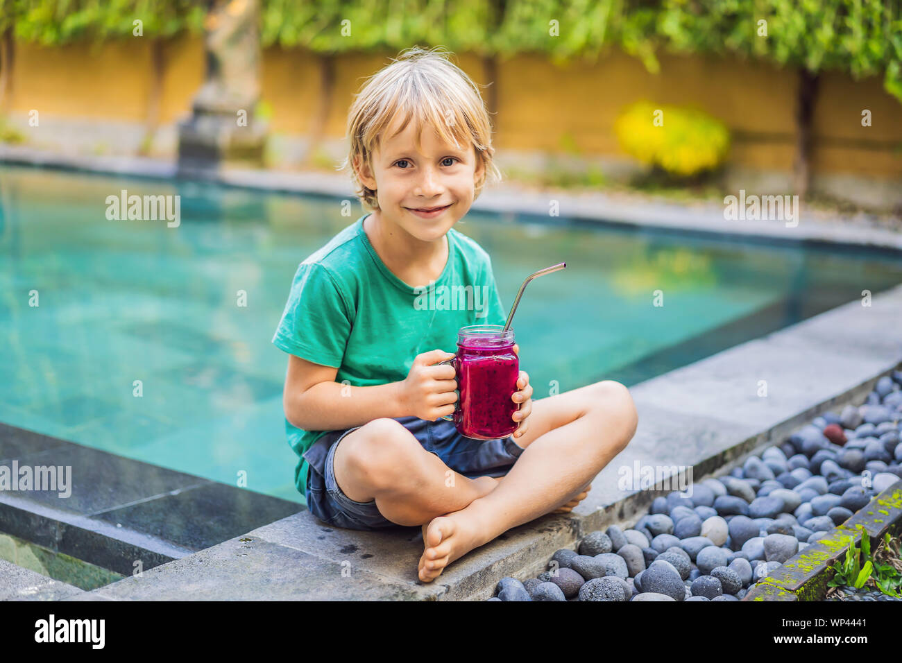 Boy drinks dragon fruit smoothie with steel drinking straw by the pool