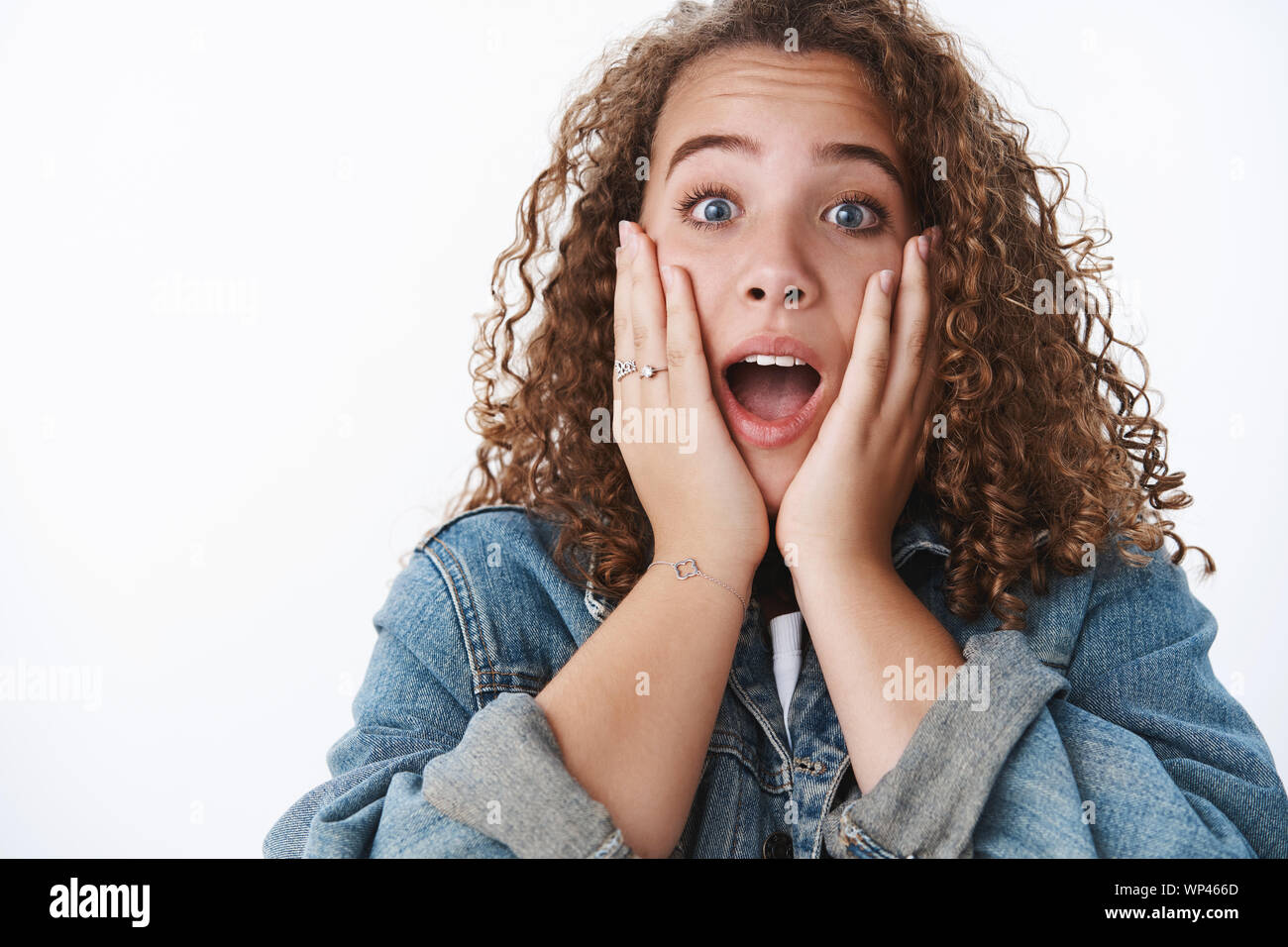 Close-up amused charismatic cute curly-haired chubby woman open mouth surprised amazed touch cheeks impressed standing speechless astonished awesome n Stock Photo