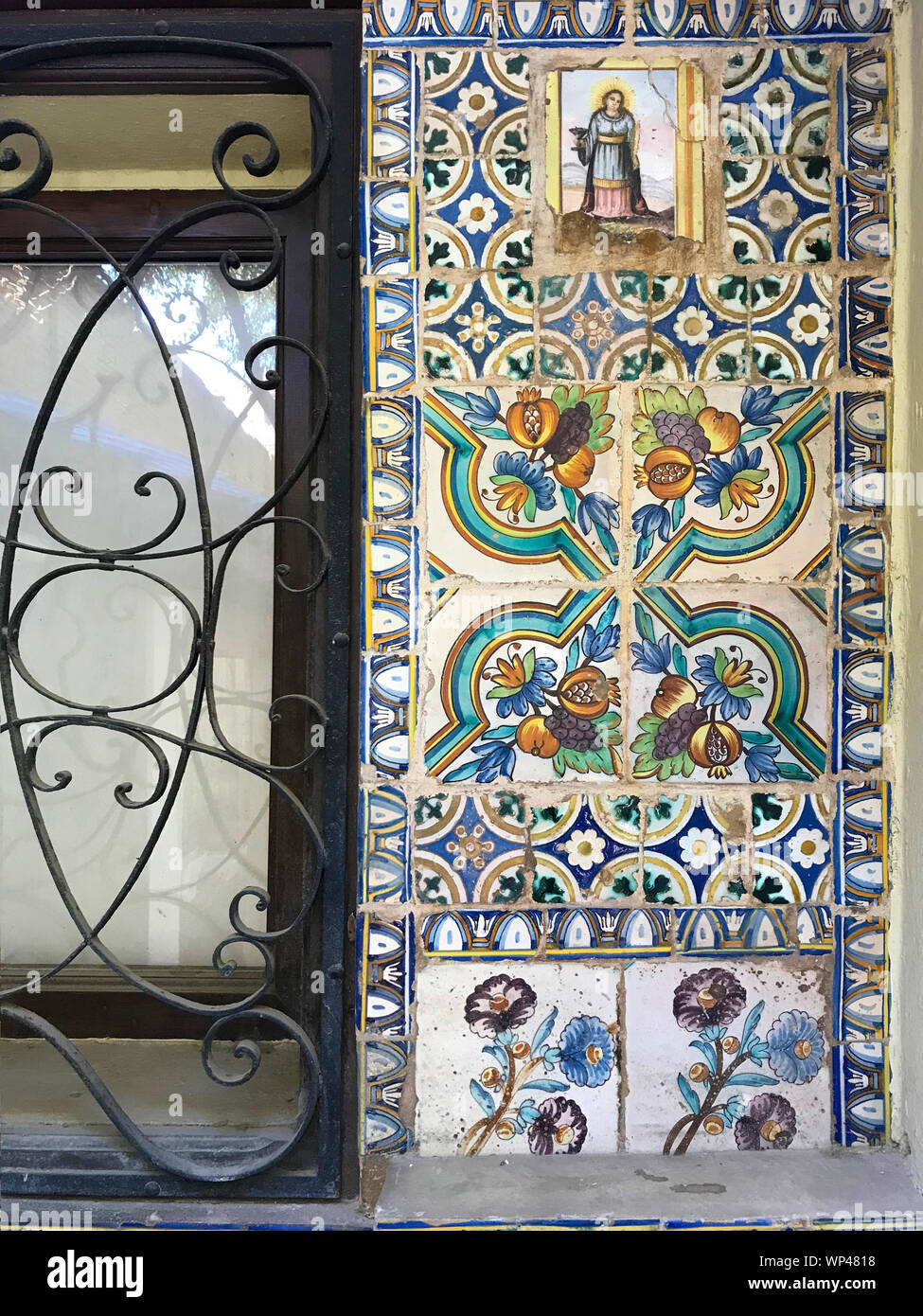 Spanish tiles next to an ironwork window in an outdoor public courtyard in Valencia, Spain, depicting, flowers, fruits and a woman Stock Photo