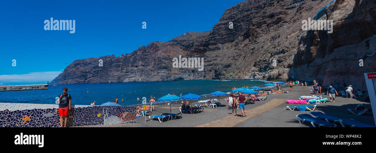 Los Gigantes Beach, Tenerife, Canary Islands. 8 October 2018: Sunbathing tourists enjoying October sunshine on the black sand beach Stock Photo