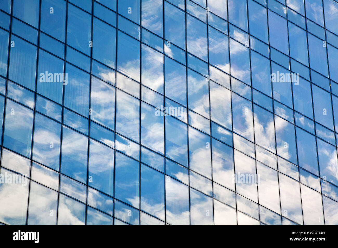 Glass mirror skyscraper wall with blue sky and white clouds reflection