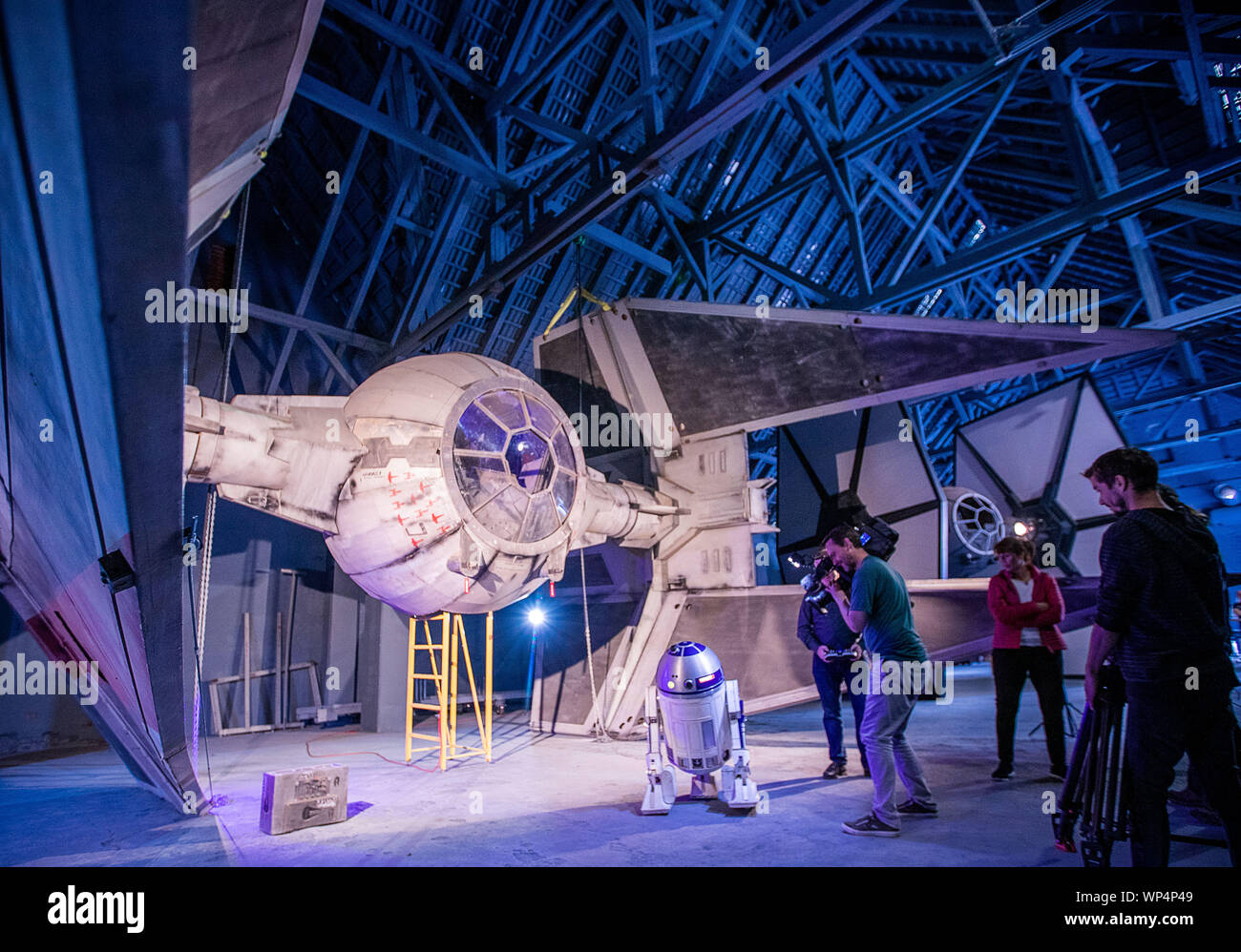 Dassow, Germany. 07th Sep, 2019. A camera team shoots in the hangar of the fan project 'Outpost One' in front of the replica of the space interceptor Tie Intercepter. The 1,300 square metre exhibition will be officially opened this weekend. With attention to detail and perfectionism, space fans have created a gigantic 'Star Wars' world. The visitor walks through 29 reconstructed set scenes of the cult film series. Since the beginning of July, trained staff has been guiding groups of visitors through the exhibition. A good 3000 visitors came during the 'preview phase'. Stock Photo