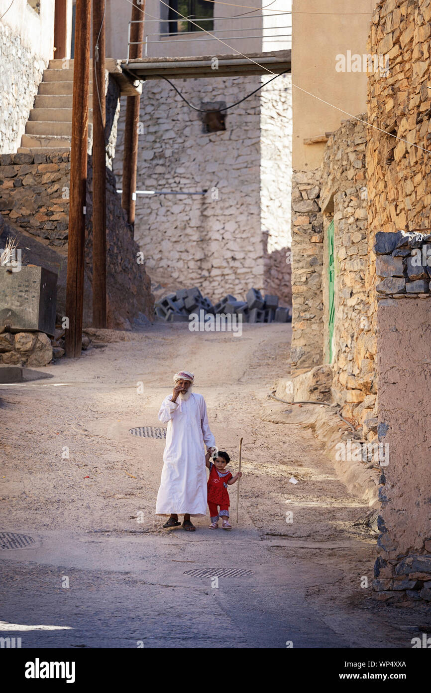 Grandfather and little girl holding hands while walking on a idyllic street of a village near Nizwa, Oman Stock Photo