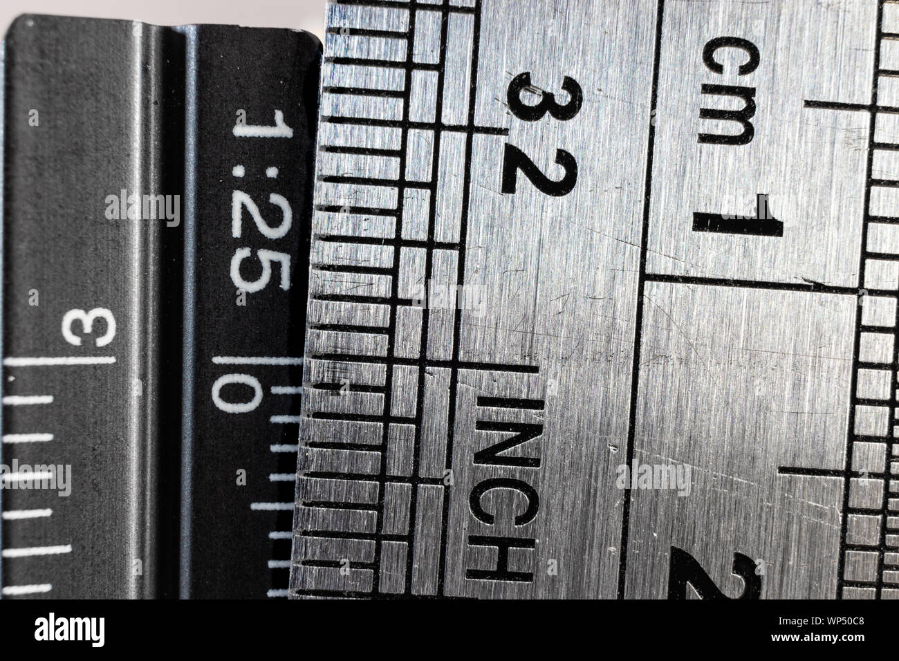 Close-up picture of two steel rulers showing the size difference between inches and centimeters. Conceptual british and metric system comparison. Stock Photo