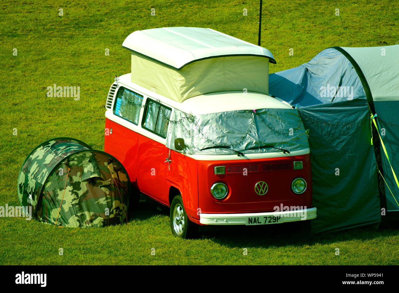 An old Volkswagen camper van with modern tents camping in a field in Chester Stock Photo
