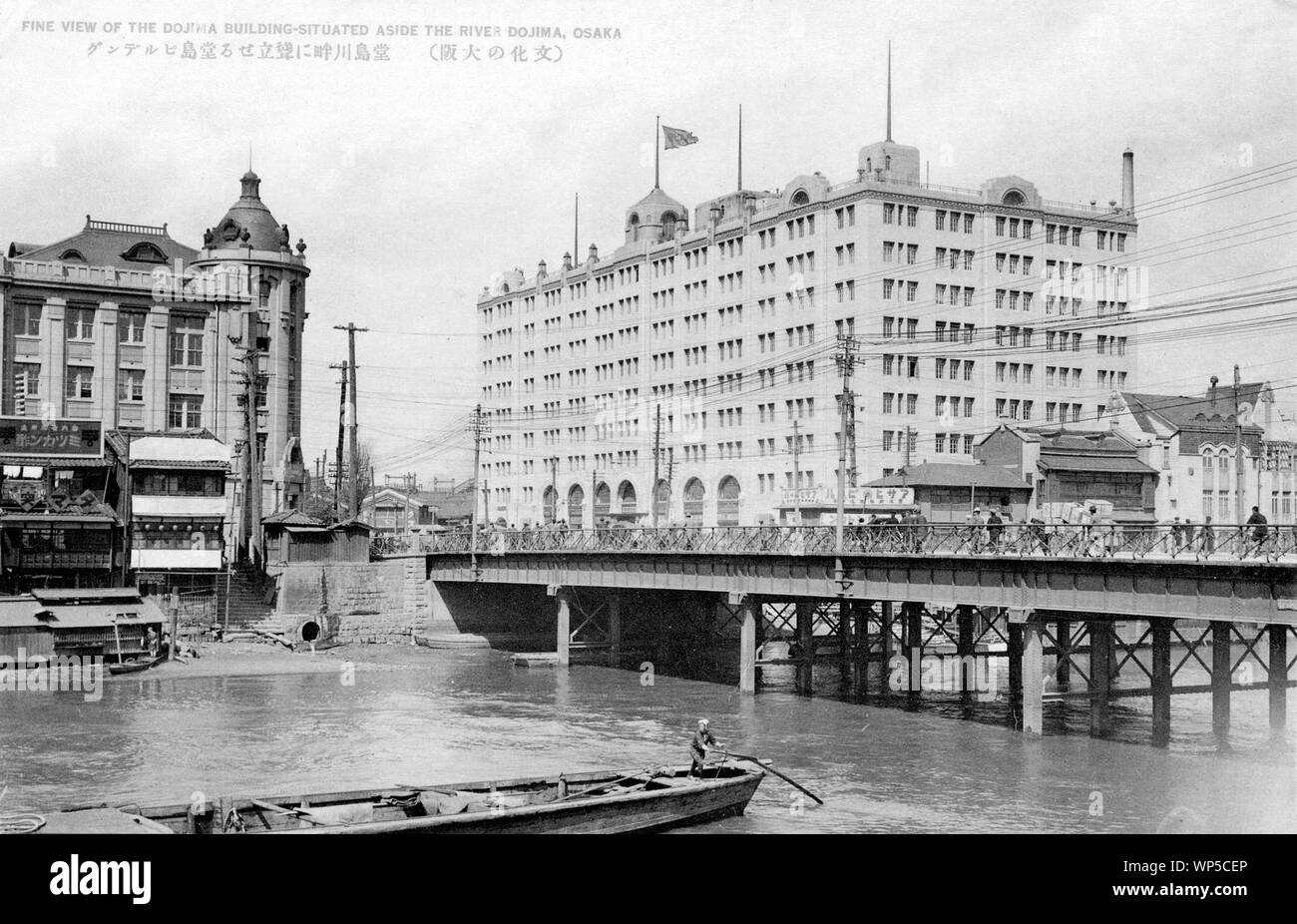 [ 1920s Japan - Oebashi Bridge in Osaka ] —   Oebashi Bridge over the Dojima River in Osaka.  The large building is the Dojima Building, constructed in 1923 (Taisho 12) by Takenaka Komuten. The building with the dome housed Fukutoku Seimen Hoken (福徳生命保険). It was designed by Kingo Tatsuno (辰野金吾, 1854-1919) and Yasushi Kataoka (片岡安, 1876-1946) and opened in 1919 (Taisho 8).  The steel bridge on this photo was built in 1910 (Meiji 43). Construction of the current stone bridge was started in 1930 (Showa 5).  This effectively dates this photo to the 1920s.  20th century vintage postcard. Stock Photo