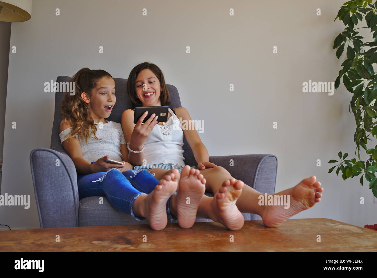 Two sisters watching videos on a smartphone together. Stock Photo