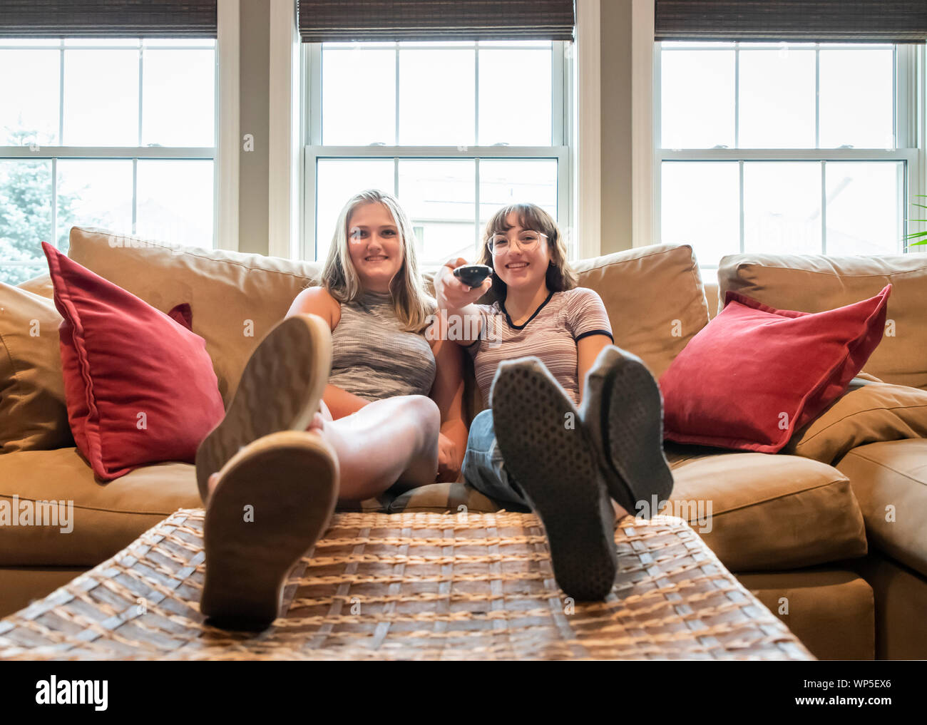 Two teenage girls sitting on couch with feet up watching tv together. Stock Photo