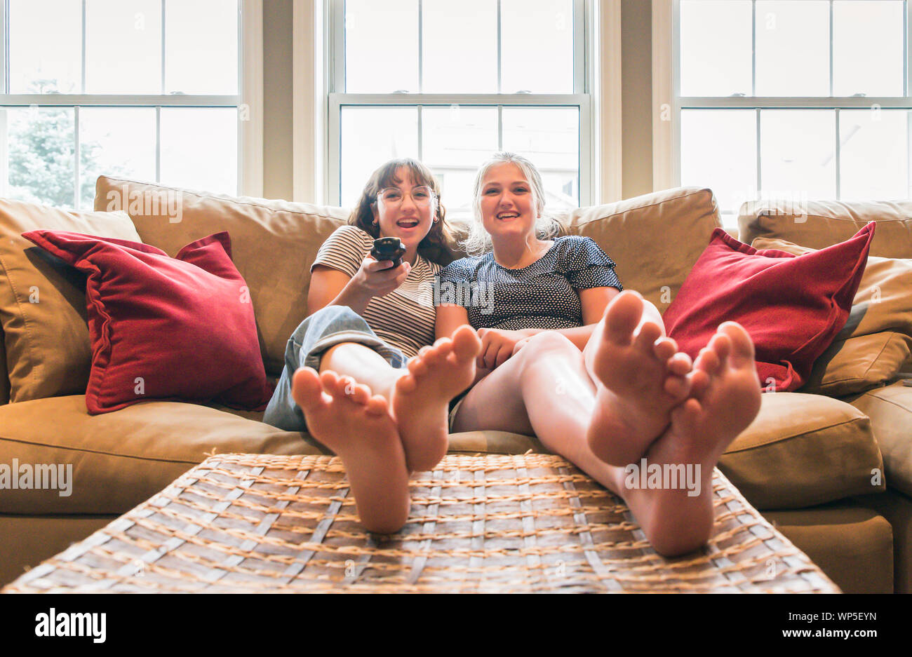 Two teenage girls sitting on a couch with feet up watching television. Stock Photo