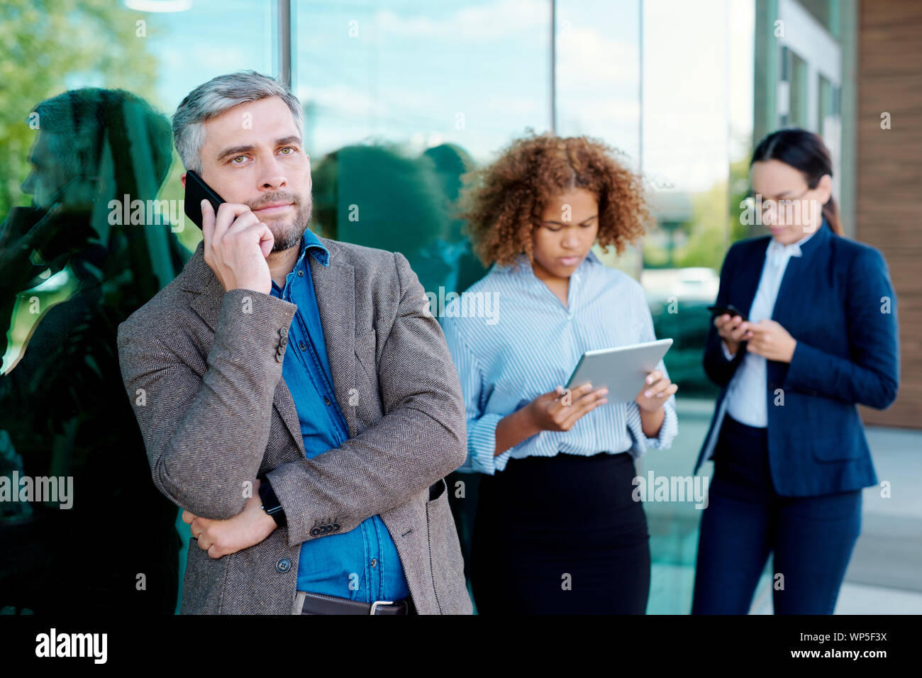 Serious businessman talking on smartphone while standing by office building Stock Photo