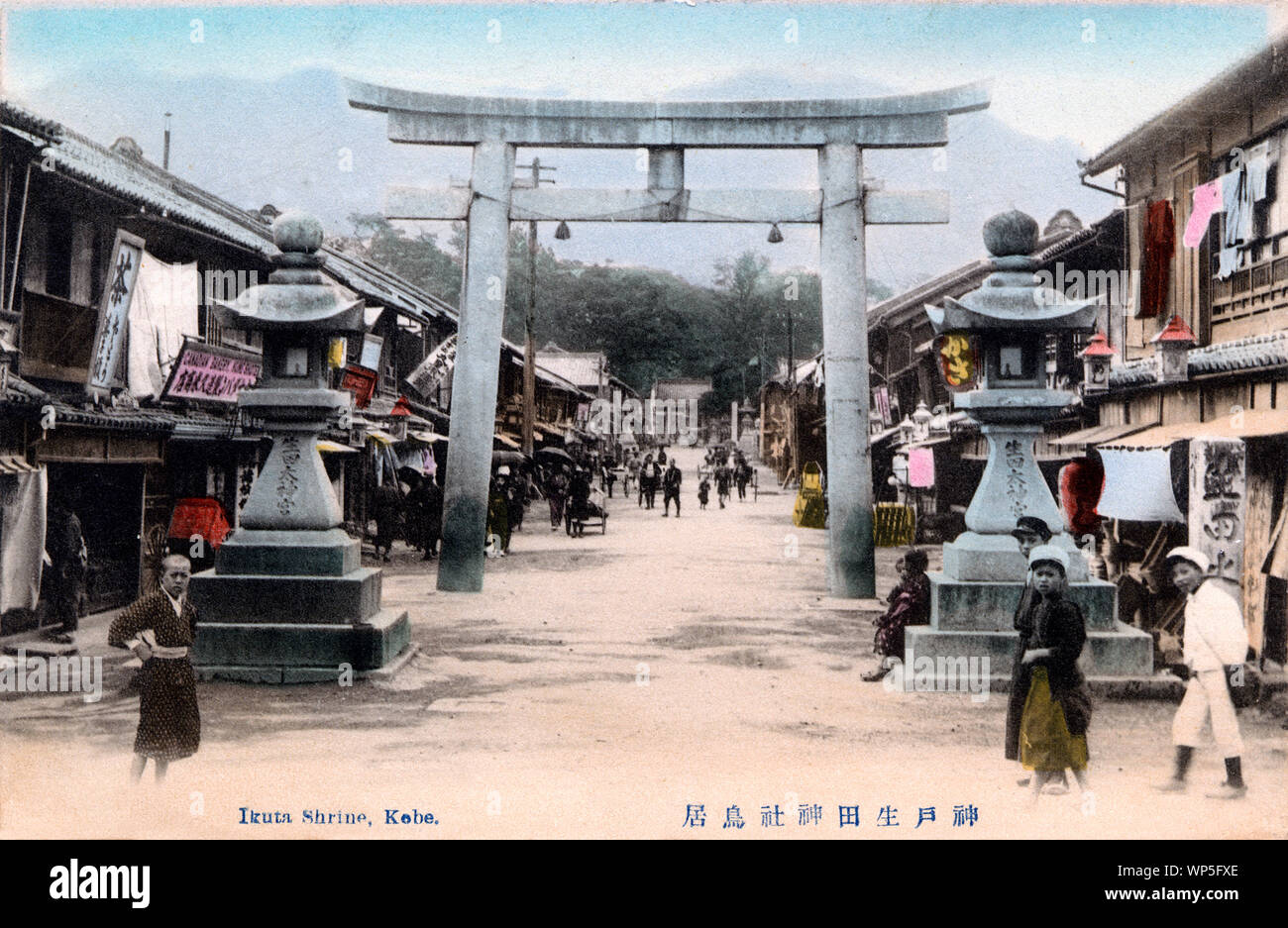 [ 1910s Japan - Sacred Torii Gate at Kobe's Ikuta Shrine ] —   Stone lanterns and a scared torii gate at the entrance way to Ikuta Jinja, a Shinto shrine in Kobe, Hyogo Prefecture.  Lots of shops line the street. The shrine is among the oldest shrines in Japan and is mentioned in the Nihon Shoki, the second oldest book of classical Japanese history.  The Battle of Ichi-no-Tani (1184) took place in and around Ikuta Shrine.  20th century vintage postcard. Stock Photo