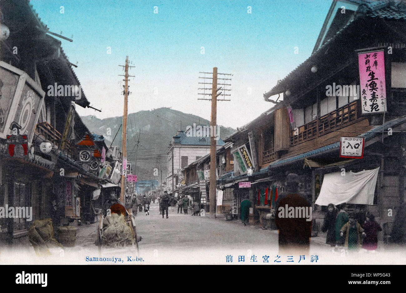[ 1910s Japan - Shopping Street in Sannomiya, Kobe ] —   This postcard of Sannomiya in Kobe, Hyogo Prefecture shows Ikuta-mae, the street leading to the shinto shrine Ikuta Jinja.  In the background the shrine’s torii can be seen. One Western style building made of stone stands out among the otherwise traditional wooden architecture.  When Kobe opened its port for trade in 1868 (Meiji 1), this was a beautiful sand-road that lead from the shrine to the sea and was lined on both sides with plum and cherry trees and countless stone lanterns.  20th century vintage postcard. Stock Photo
