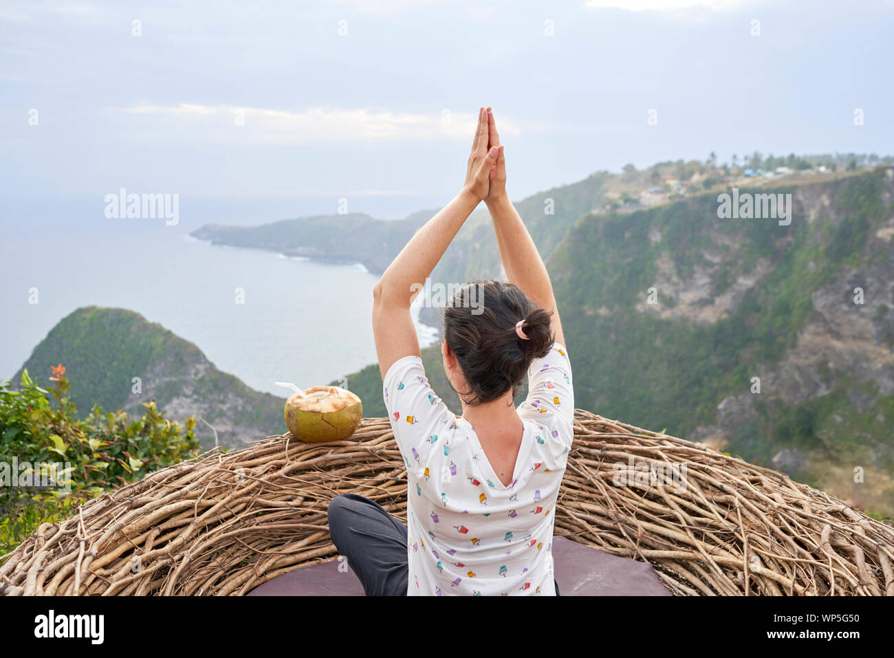 Young Woman Taking A Break And Drinking A Coconut Inside A Nest In Front Of The Sea, Bali, Indonesia Stock Photo