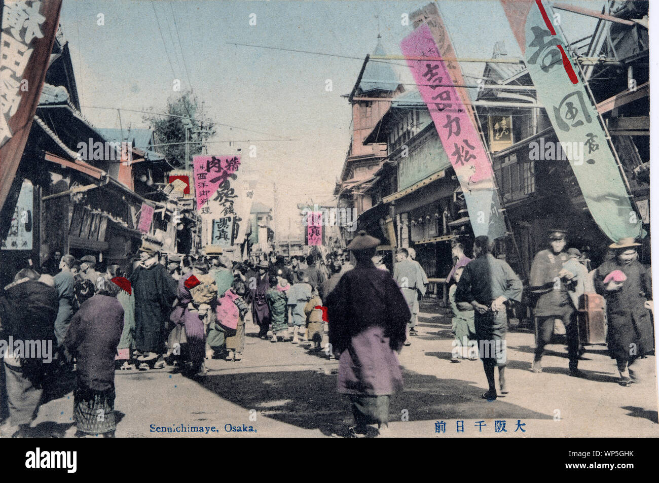 [ 1910s Japan - Sennichimae Entertainment District in Osaka ] —   People walk under flags at Sennichimae, Osaka.  Together with Dotonbori, Sennichimae was Osaka’s main entertainment area since the Edo Period (1603-1868).  20th century vintage postcard. Stock Photo