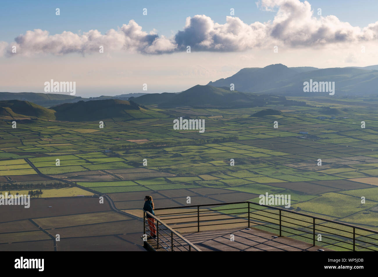 A young woman enjoying and observing the view of fields from the viewing platform of Miradouro da Serra do Cume on Terceira island at a beautiful suns Stock Photo