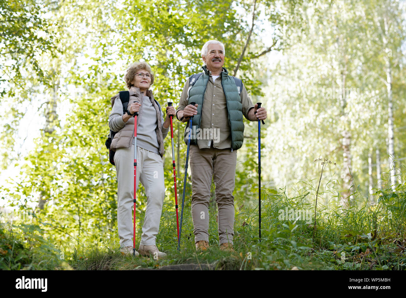 Mature active man and woman with trekking sticks standing among green trees Stock Photo
