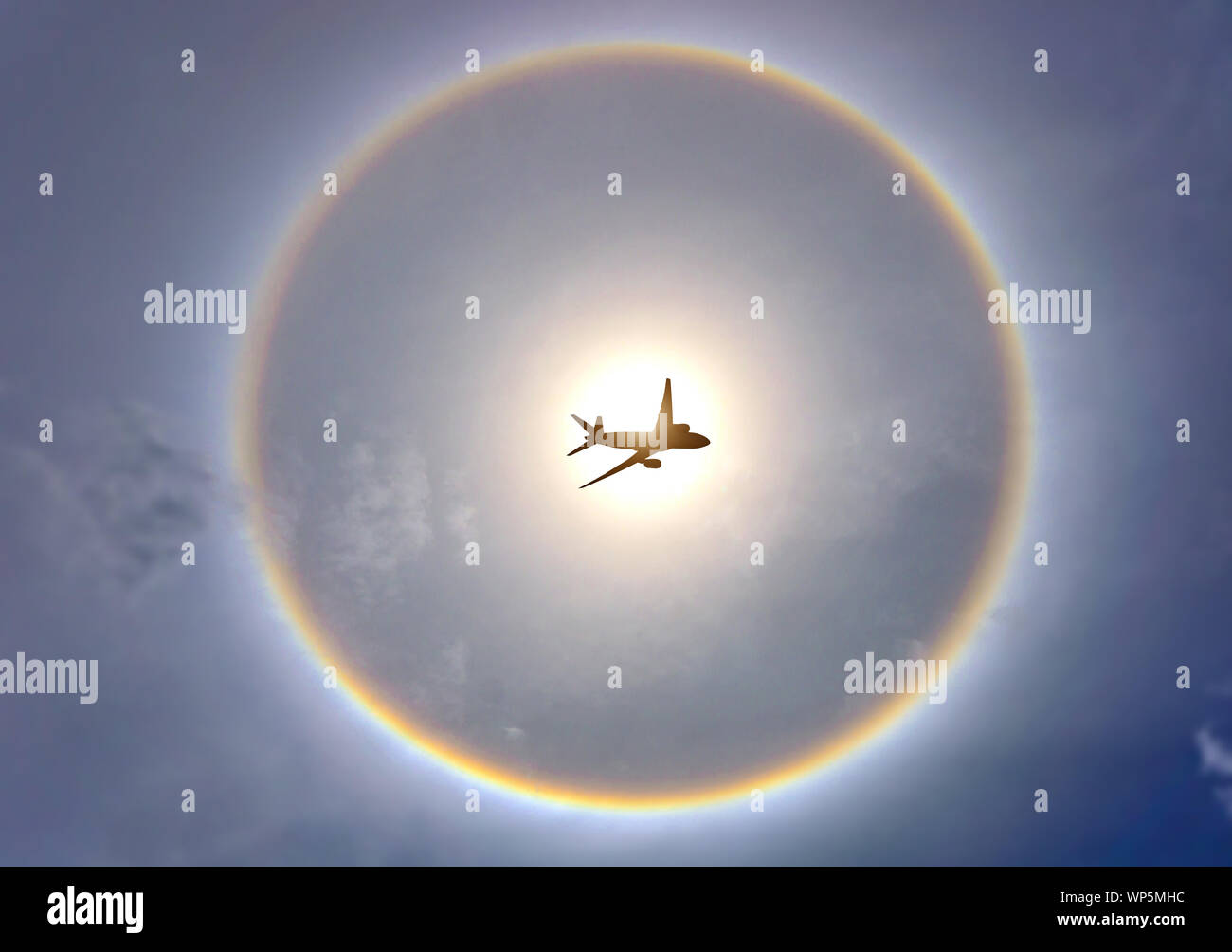 The plane is flying and has a rainbow background that exceeds the sun halo. Stock Photo