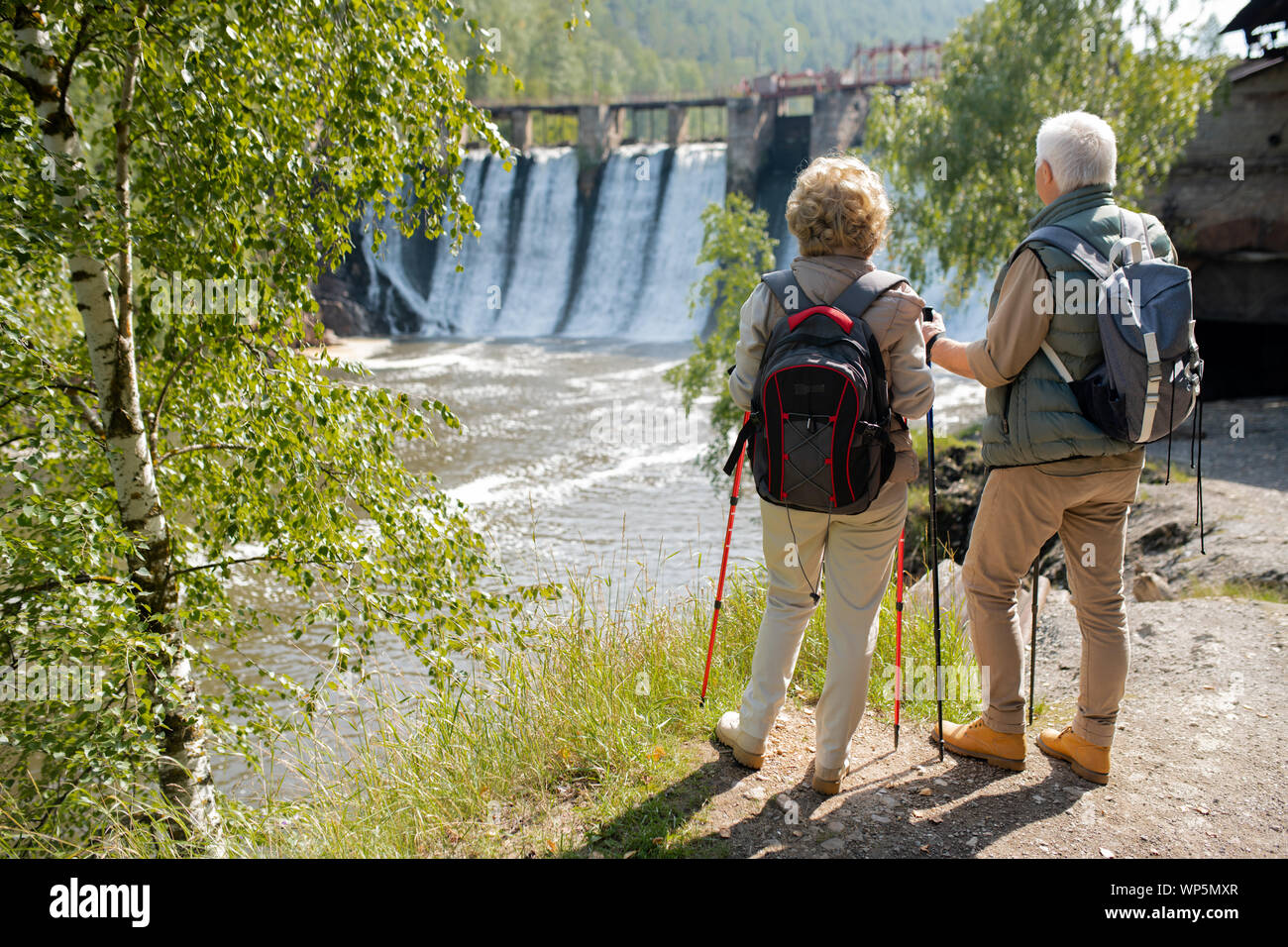 Back view of mature couple with backpacks standing on the river bank Stock Photo