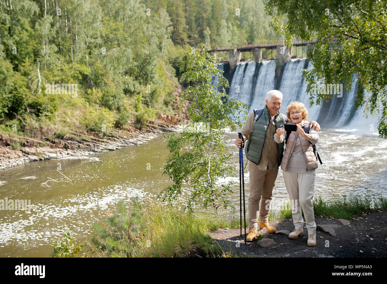 Cheerful senior couple in activewear making selfie on background of waterfalls Stock Photo
