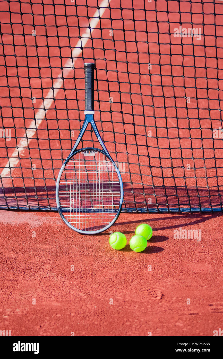 Still life of tennis balls and a racket on a red clay tennis court. Stock Photo
