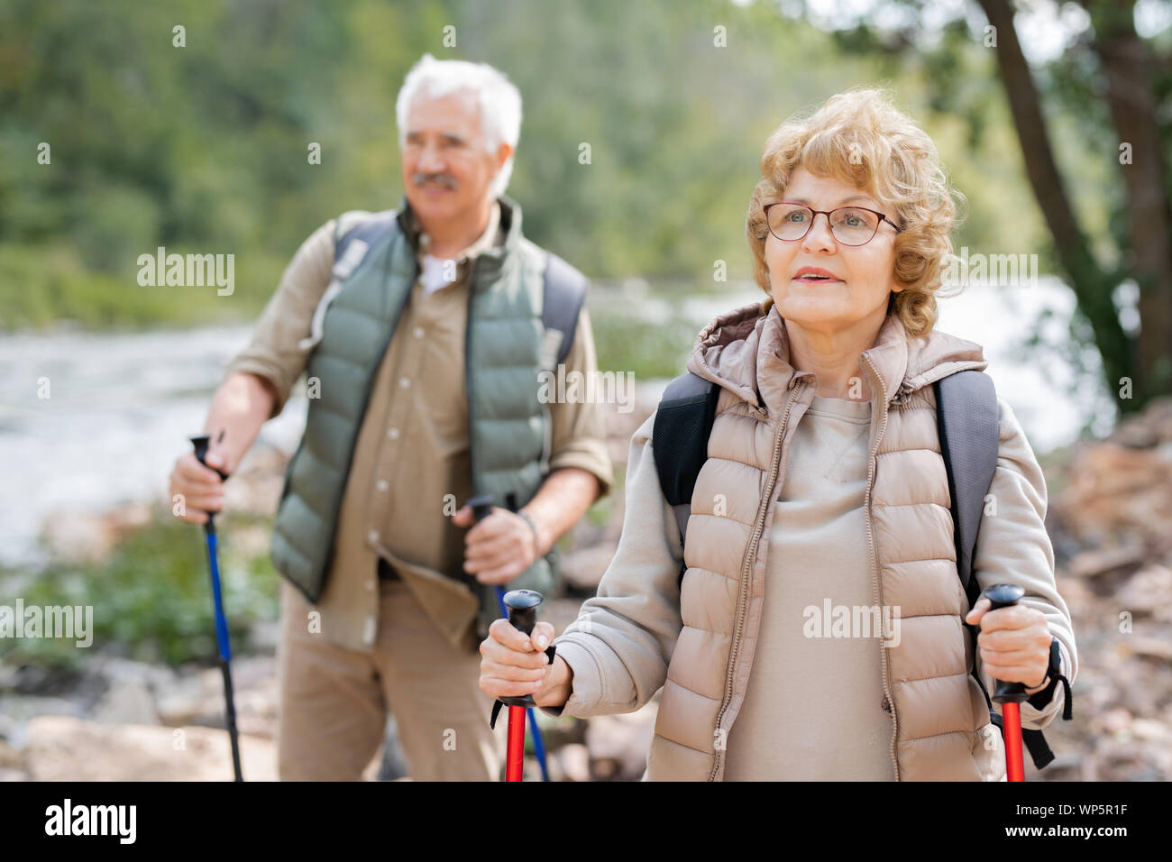 Pretty mature female hiker and her husband moving down river bank Stock Photo