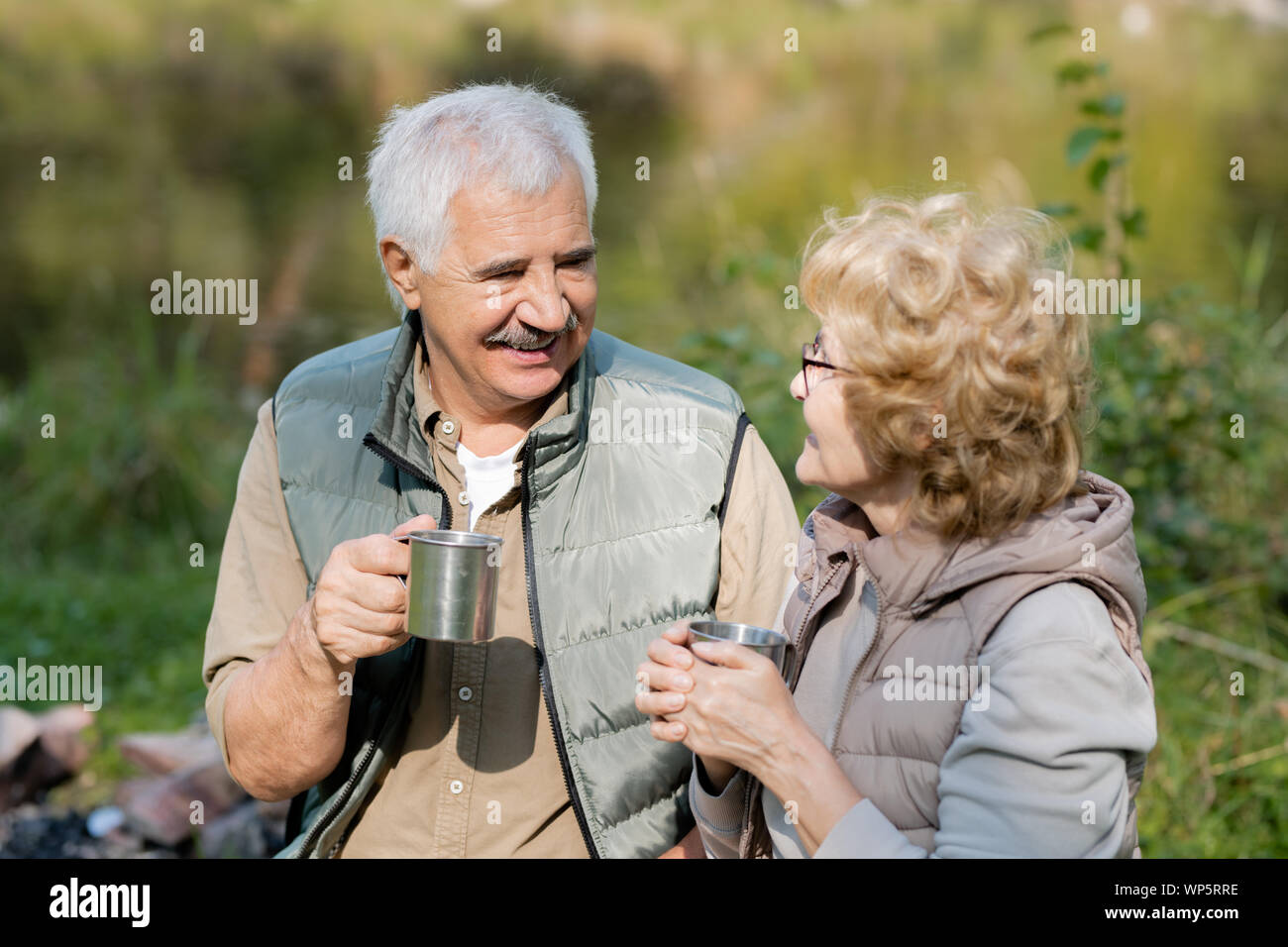 Happy mature man and his wife with tourist mugs having tea and talk Stock Photo