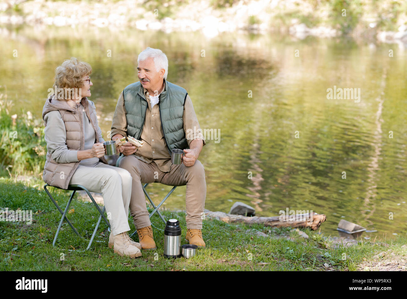 Mature affectionate man and woman in activewear having tea with sandwiches Stock Photo