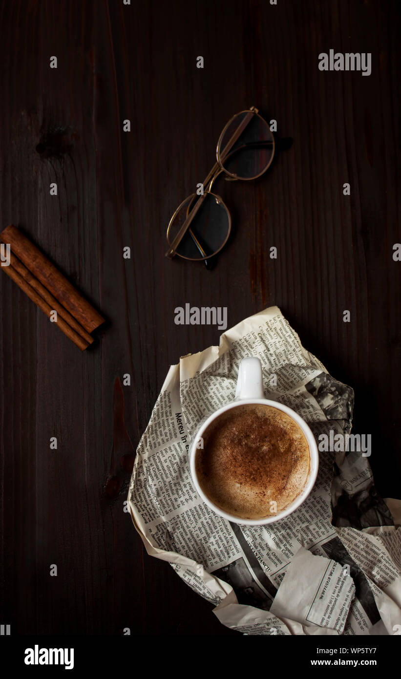 Moody view of warm cup of cappuccino, cinnamon sticks and glasses on ...