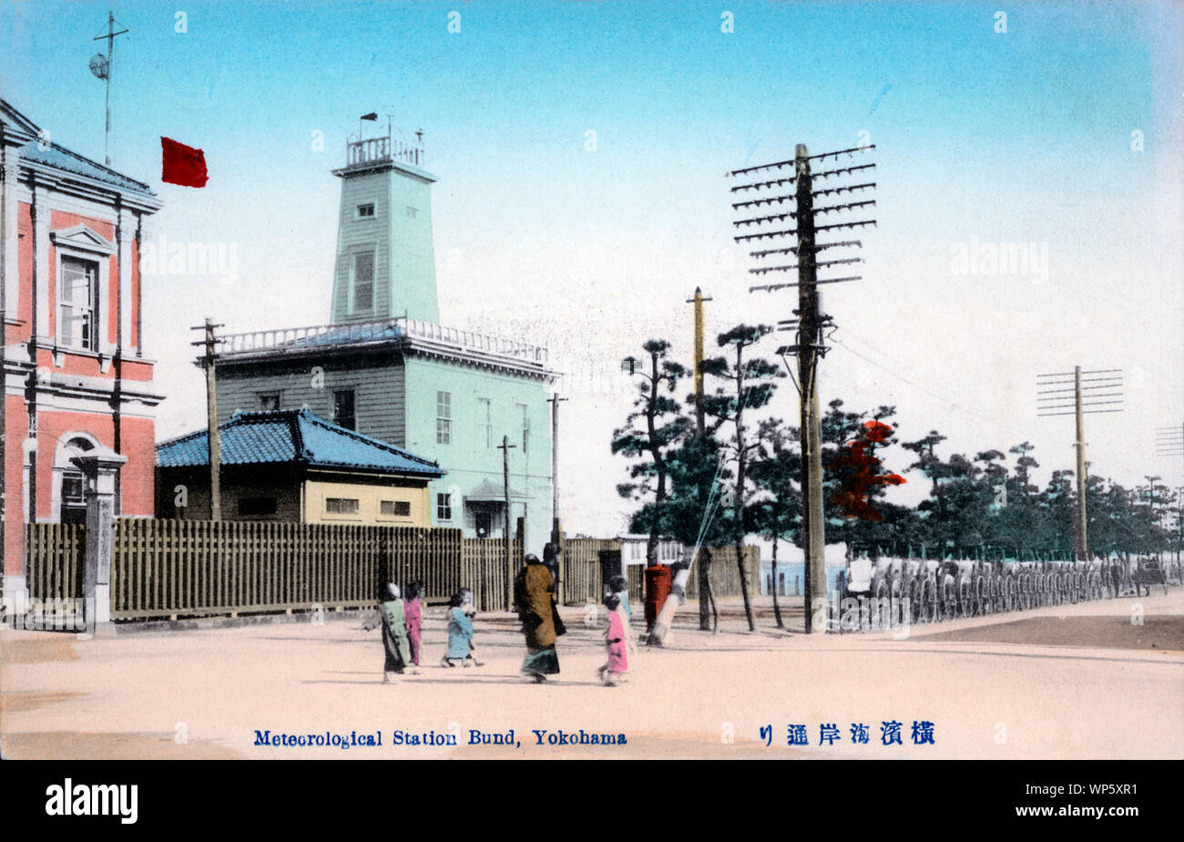 [ 1900s Japan - Meteorological Station in Yokohama Port ] —   A long row of rickshaws in front of the Meteorological Station on Kaigandori, also known as the Bund, in Yokohama, Kanagawa Prefecture.  The red brick building next to it is the Kanagawa Harbor Department (神奈川県港務部). Both buildings were located on the right of the entrance to Yokohama Pier. Therefore the many rickshaws.  20th century vintage postcard. Stock Photo