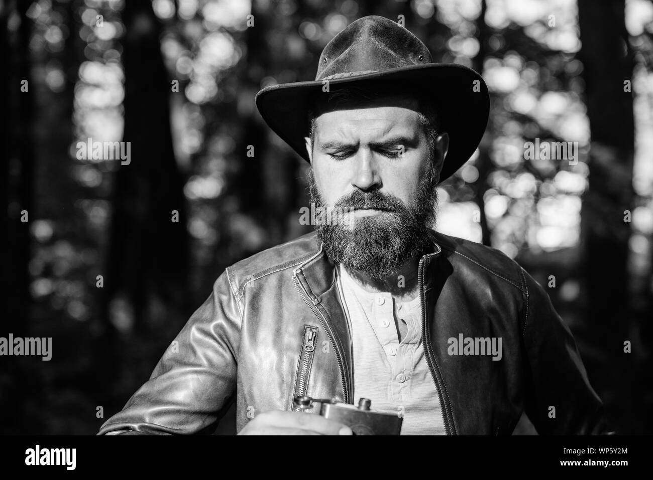 on ranch. mature male with brutal look drink alcohol from metallic flask. Bearded man in cowboy hat walk in park outdoor. man hipster relax in autumn forest. Spring sunny weather. camping and hiking. Stock Photo