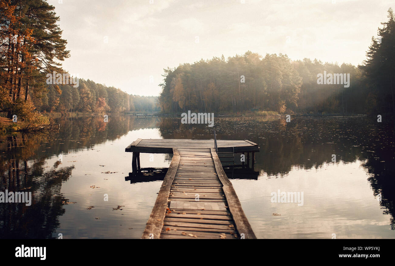 The Breath Of Autumn. Autumn foliage and fog lake in morning with boat dock Stock Photo