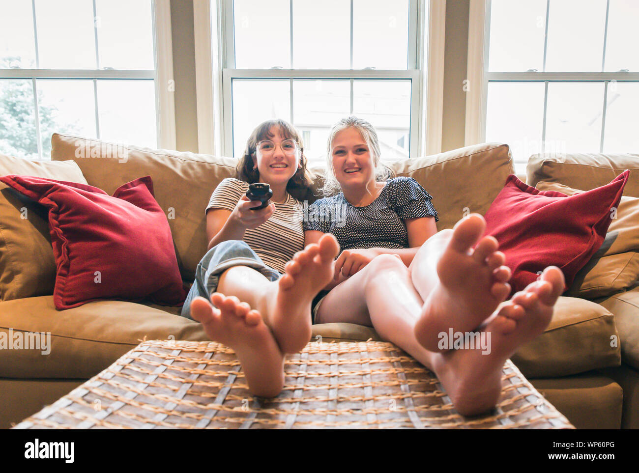 Two teenage girls sitting on couch with feet up watching television. Stock Photo