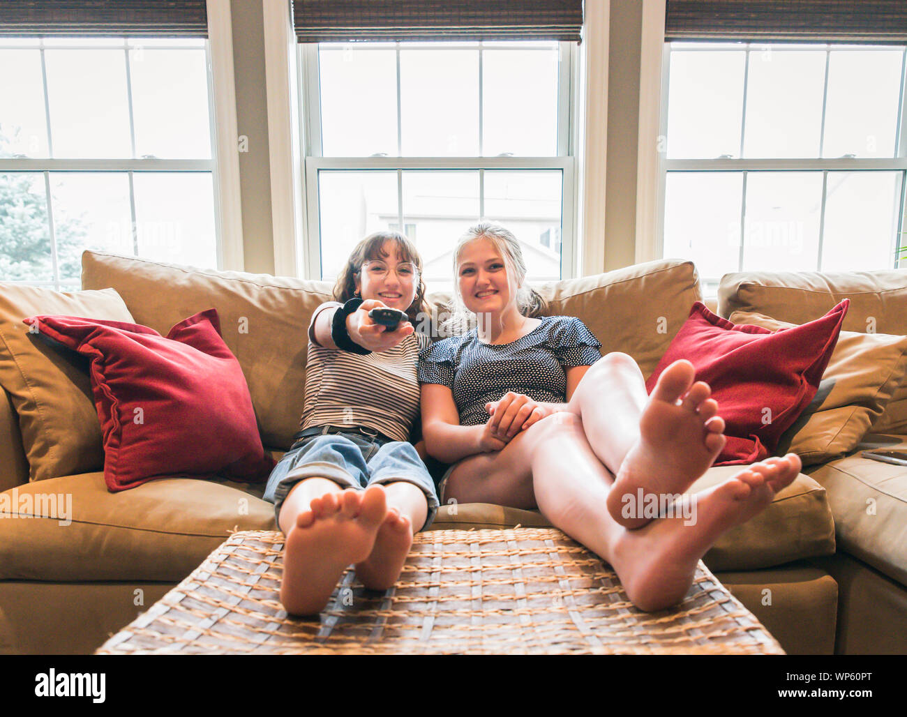 Two teenage girls sitting on a couch with feet up watching television. Stock Photo