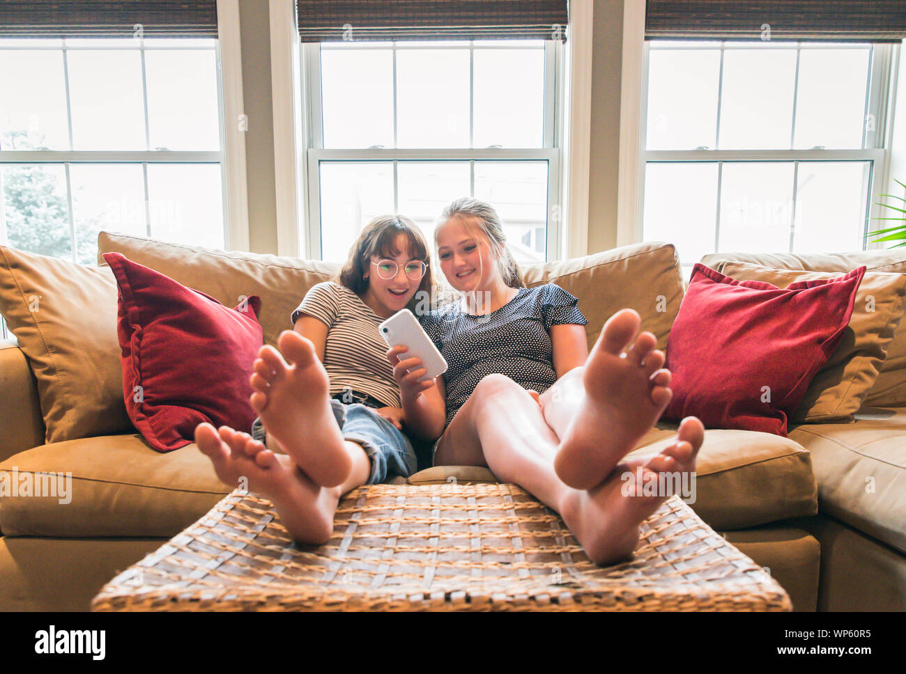 Two Teenage Girls Sitting On Couch With Feet Up Looking At Cellphone