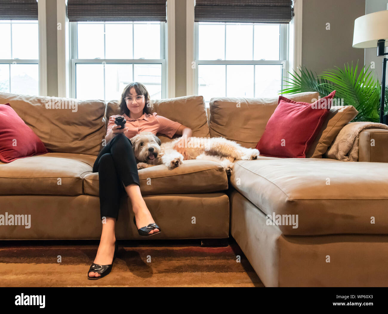 Young woman in business attire sitting on couch with dog watching tv. Stock Photo
