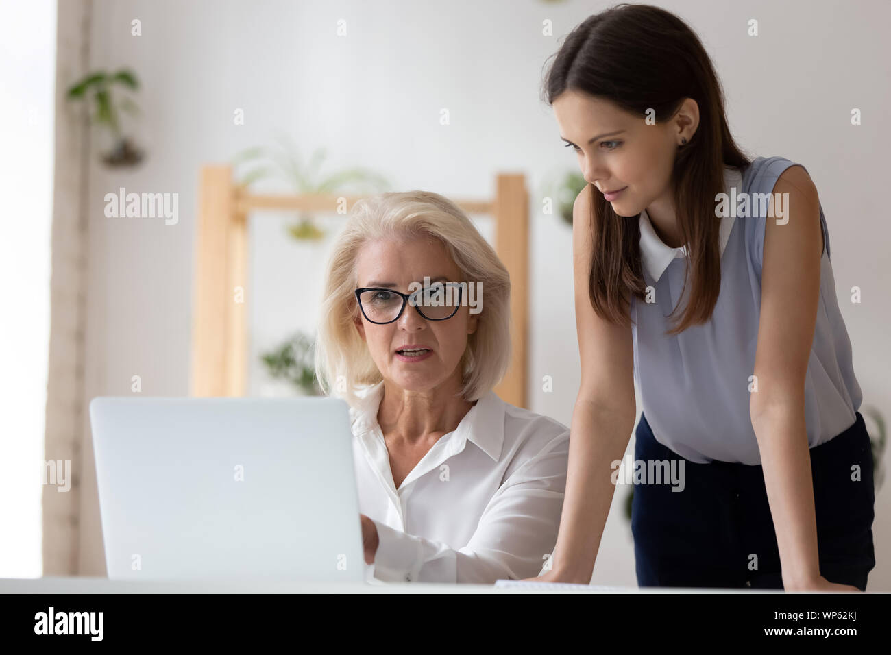Female colleagues talk sharing ideas working on laptop Stock Photo