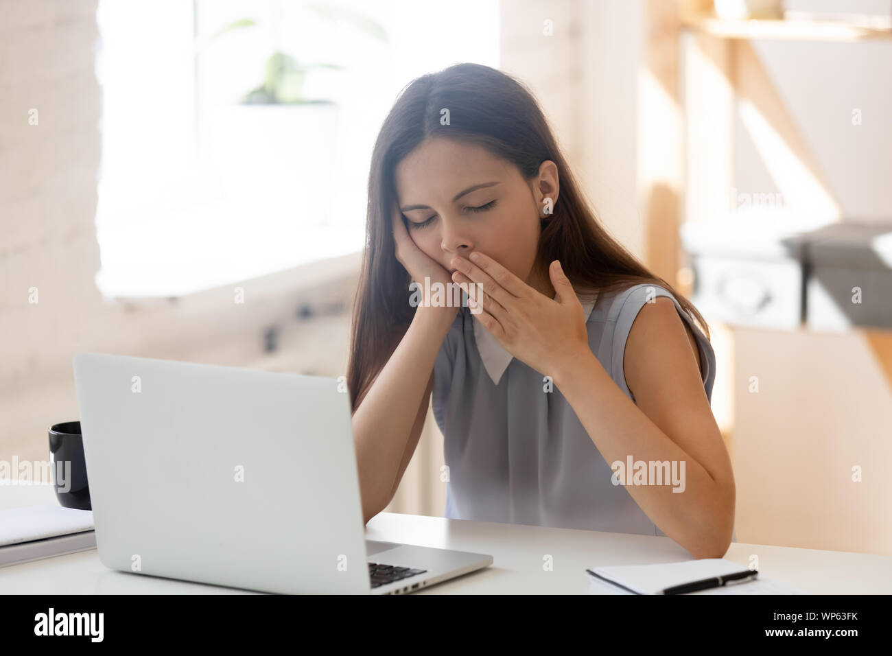 Exhausted female employee yawn feeling sleepy at workplace Stock Photo