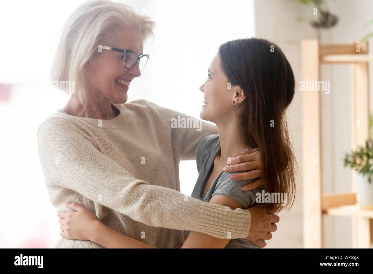 Smiling mother and daughter stand hugging looking in eyes Stock Photo